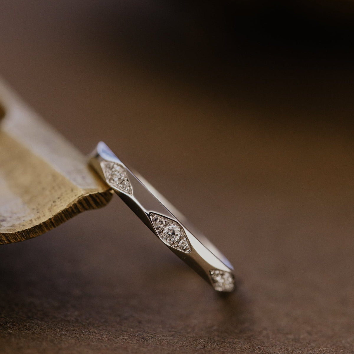Close-up of a white gold wedding band with intricate design on a brown surface.