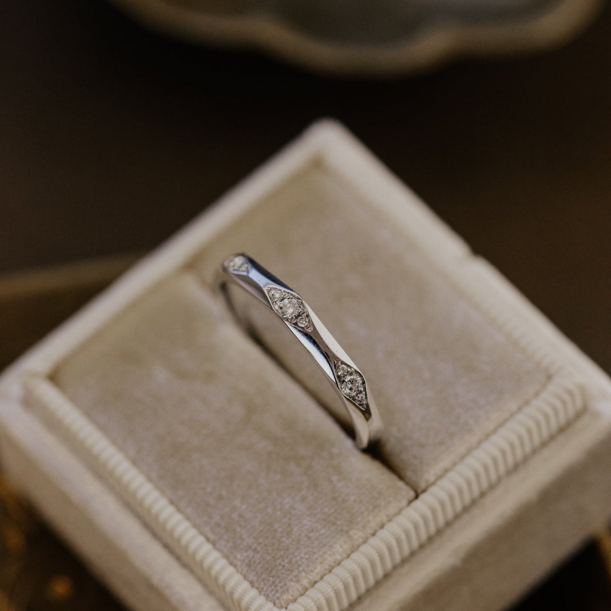White gold wedding band with gemstones in a jewelry box on a dark surface.