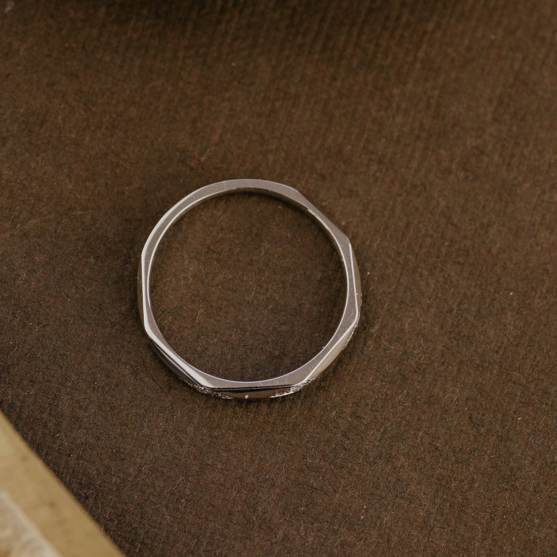 White gold wedding band on a brown leather surface.