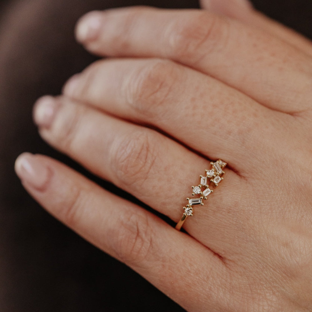 Close-up of a hand wearing a gold wedding band with diamond stones on a blurred background.