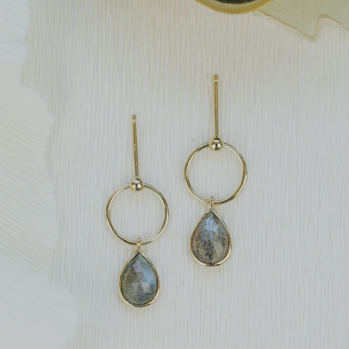 14k yellow gold pear-shaped dangle earrings with a labradorite stone on a textured background. 
