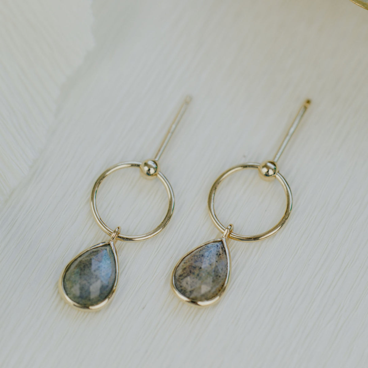 14k yellow gold pear-shaped dangle earrings with a labradorite stone on a textured background. 