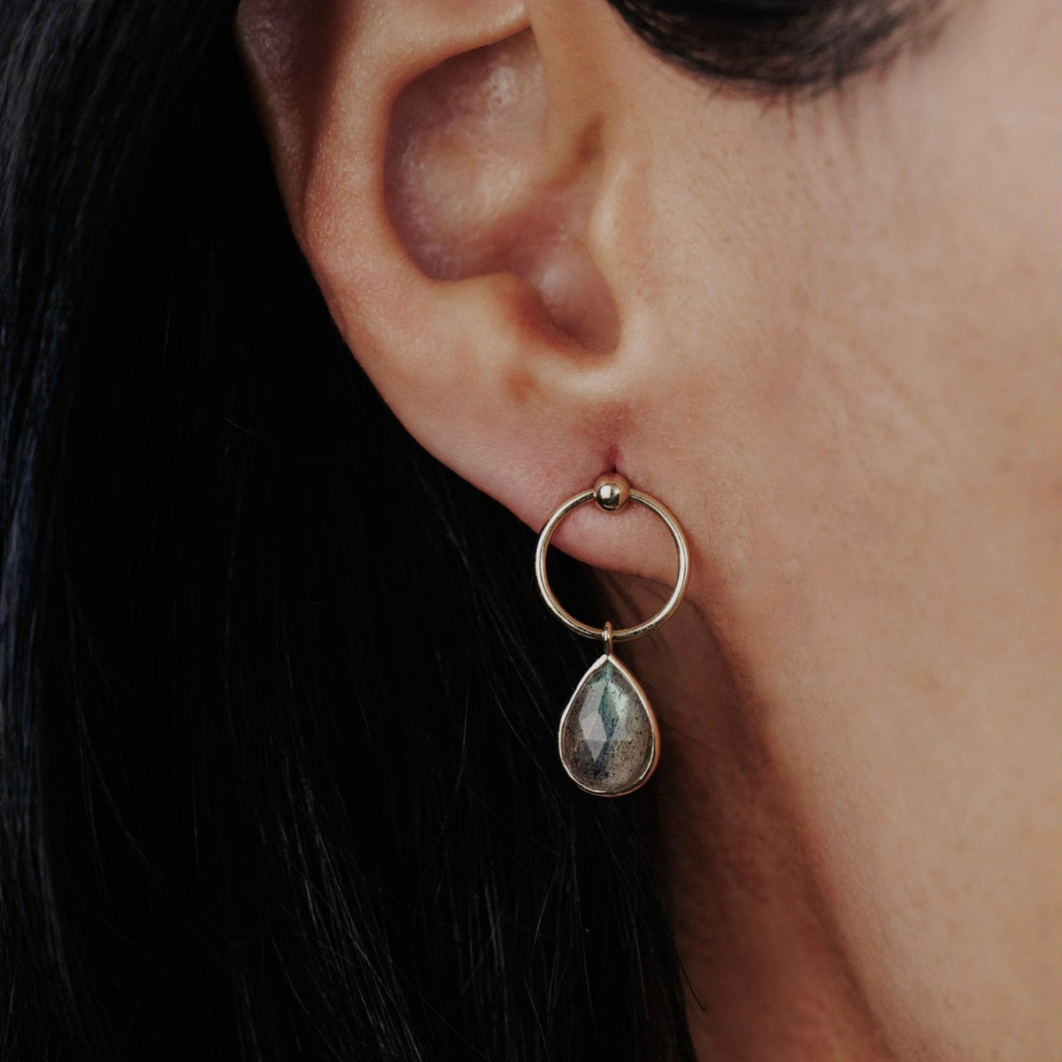 14k yellow gold pear-shaped dangle earrings with a labradorite stone showcased on a model. 