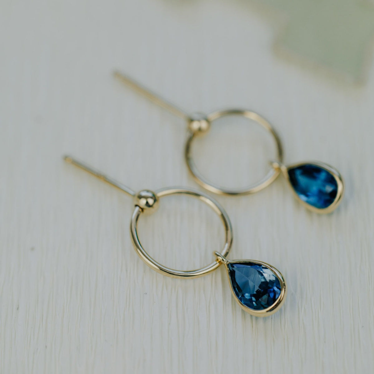 14k yellow gold pear shaped blue topaz dangle earrings on a textured background. 