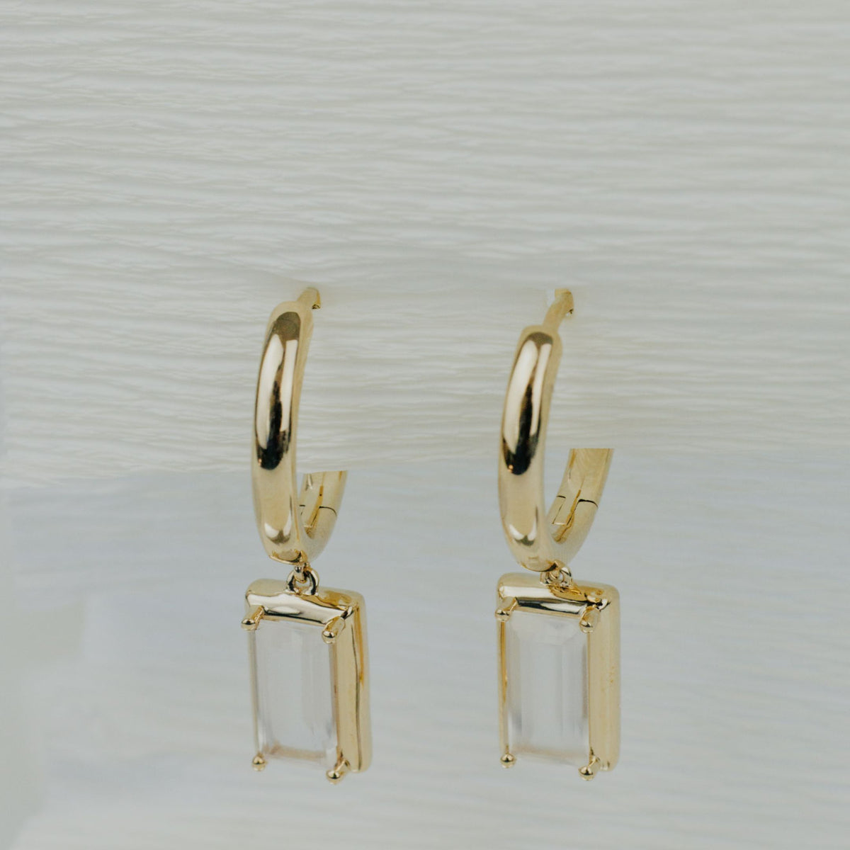 14k yellow gold emerald cut moonstone dangle earrings on a textured white background. 