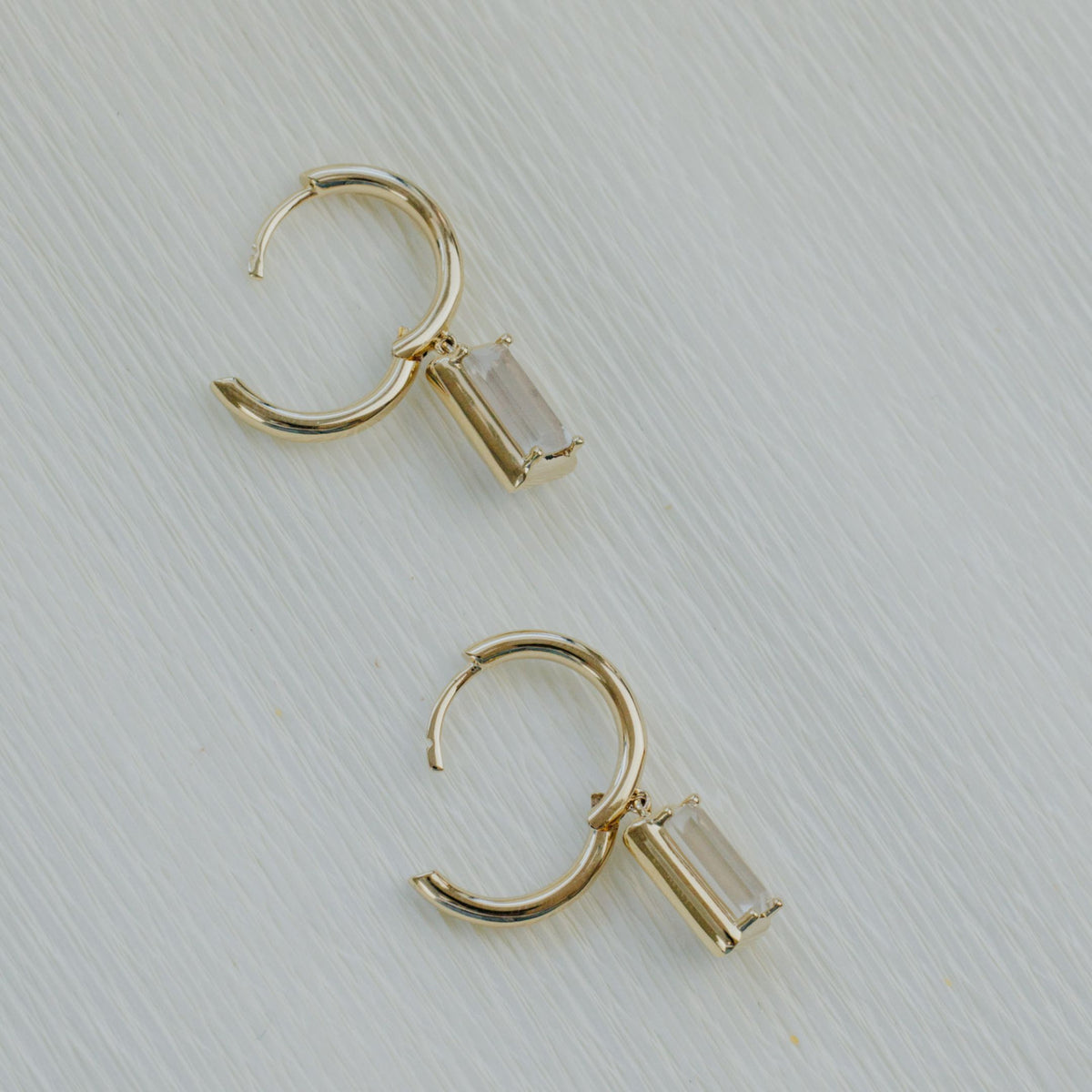 14k yellow gold emerald cut moonstone dangle earrings on a textured white background. 