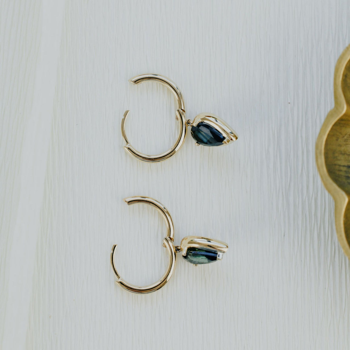 14k gold hoop dangle earrings with pear shaped green tourmaline stones on a textured white background.