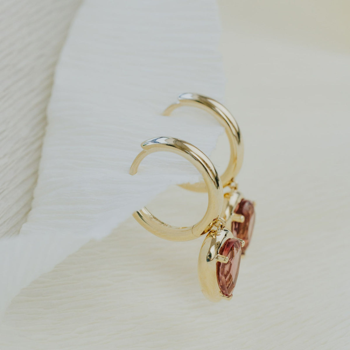 14k yellow gold pear shaped pink tourmaline dangle earrings on a textured white background. 