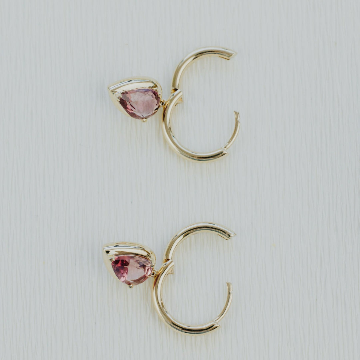 14k yellow gold pear shaped pink tourmaline dangle earrings on a textured white background. 