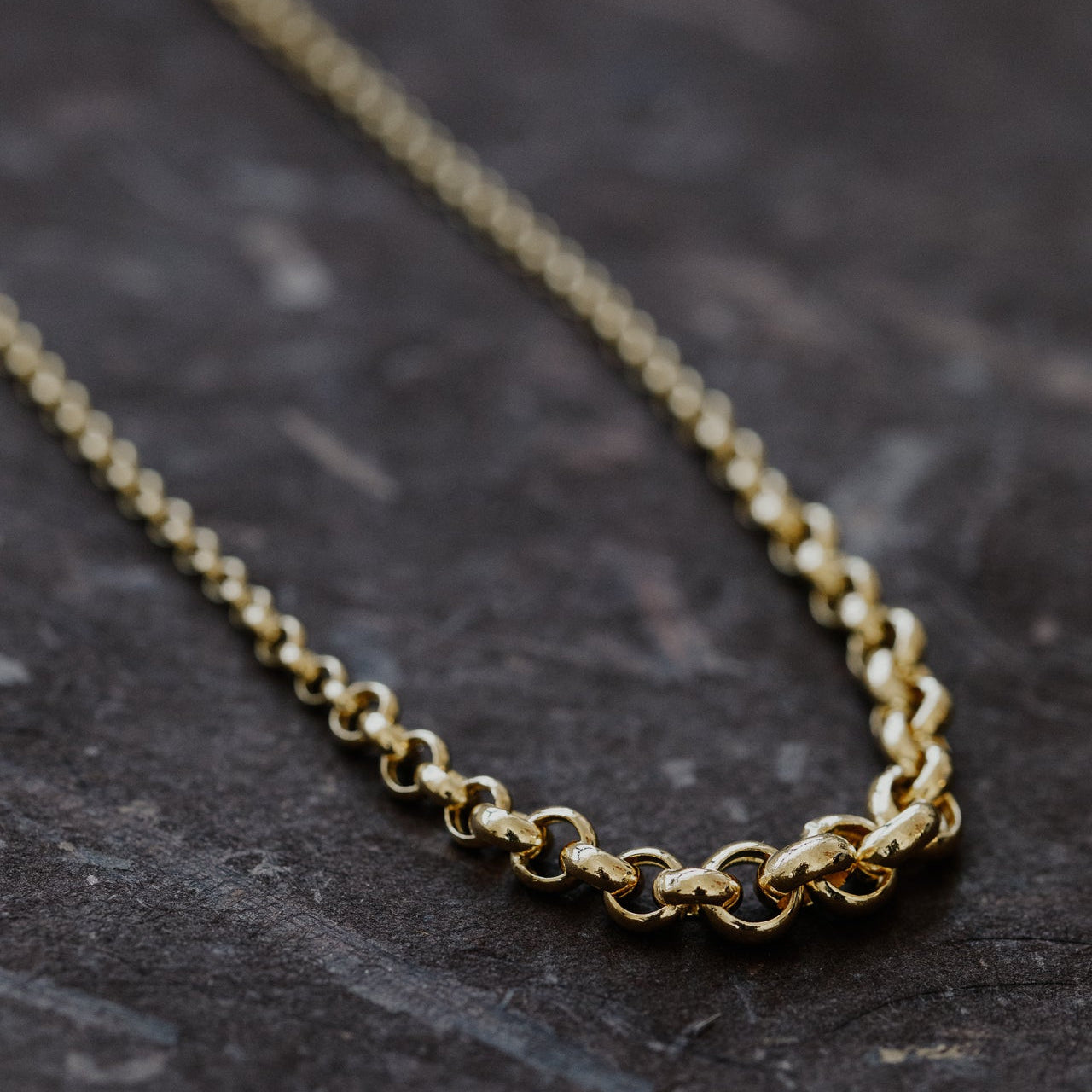 Gold chain necklace on a dark stone surface