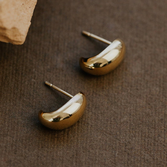 Gold earrings on a brown textured surface