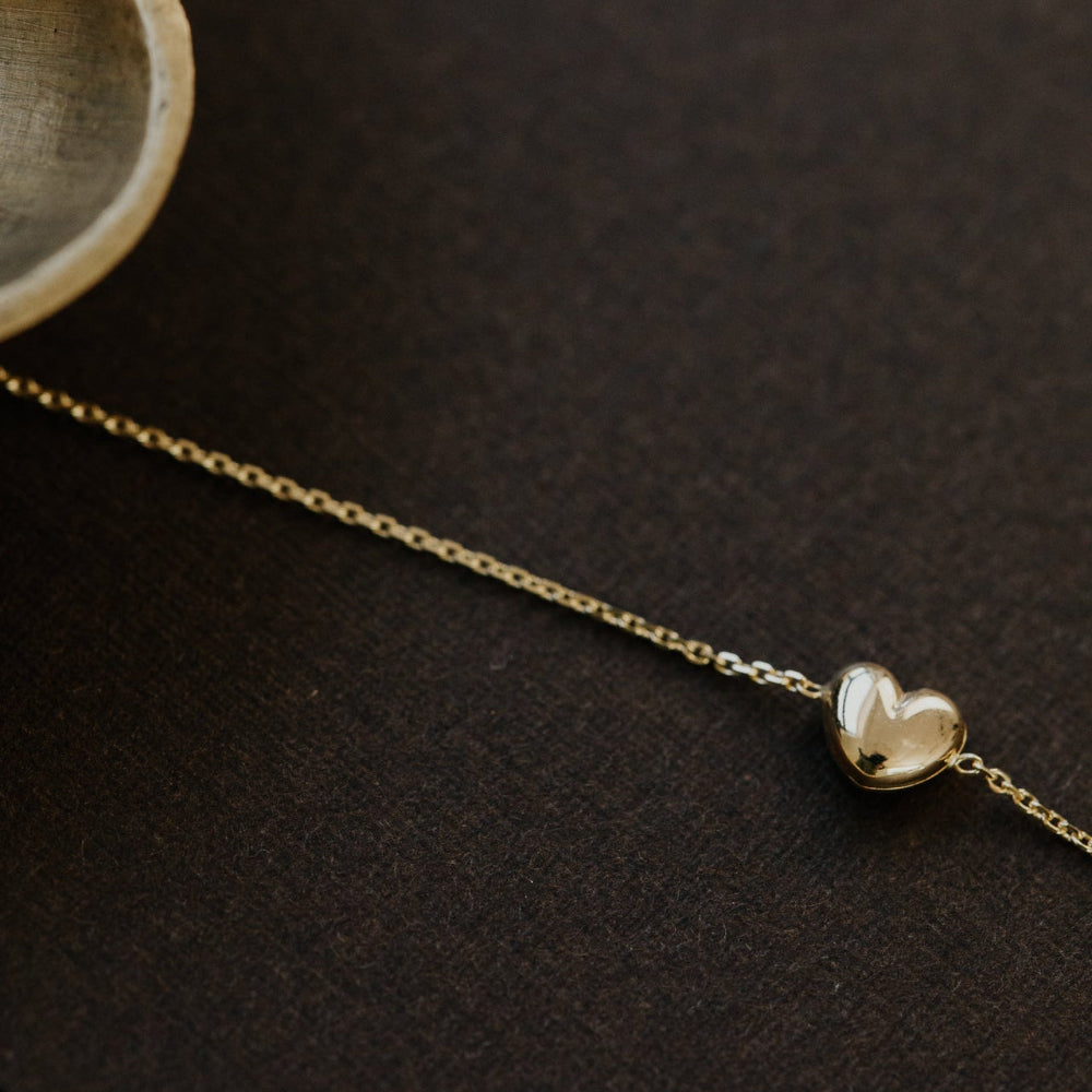 Gold heart-shaped pendant on a chain against a dark background