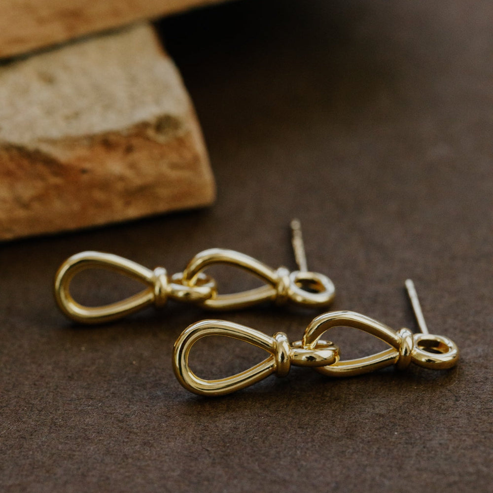 Gold infinity-shaped earrings on a brown surface