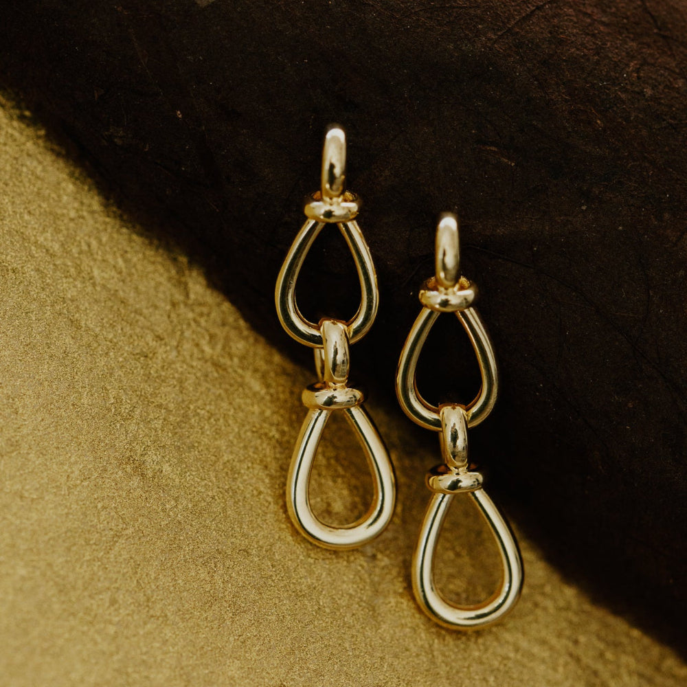 Gold teardrop earrings on a textured brown surface