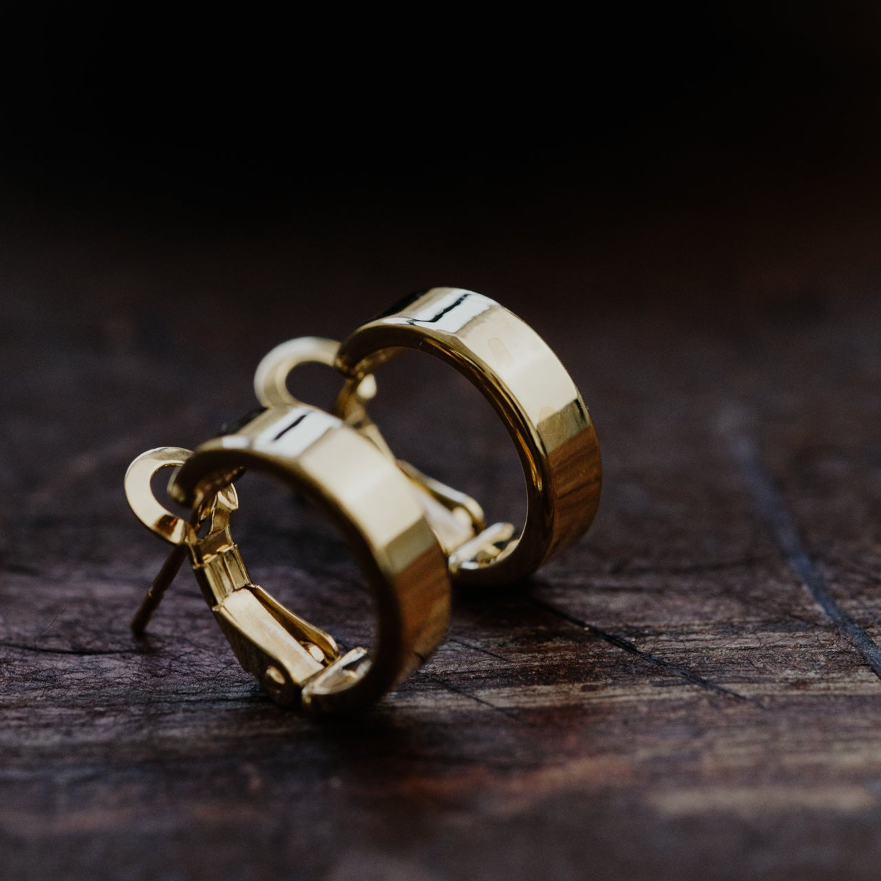 Gold hoop earrings on a dark wooden surface