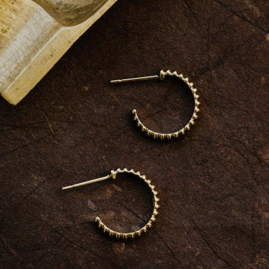Gold hoop earrings on a textured brown surface with a book in the background