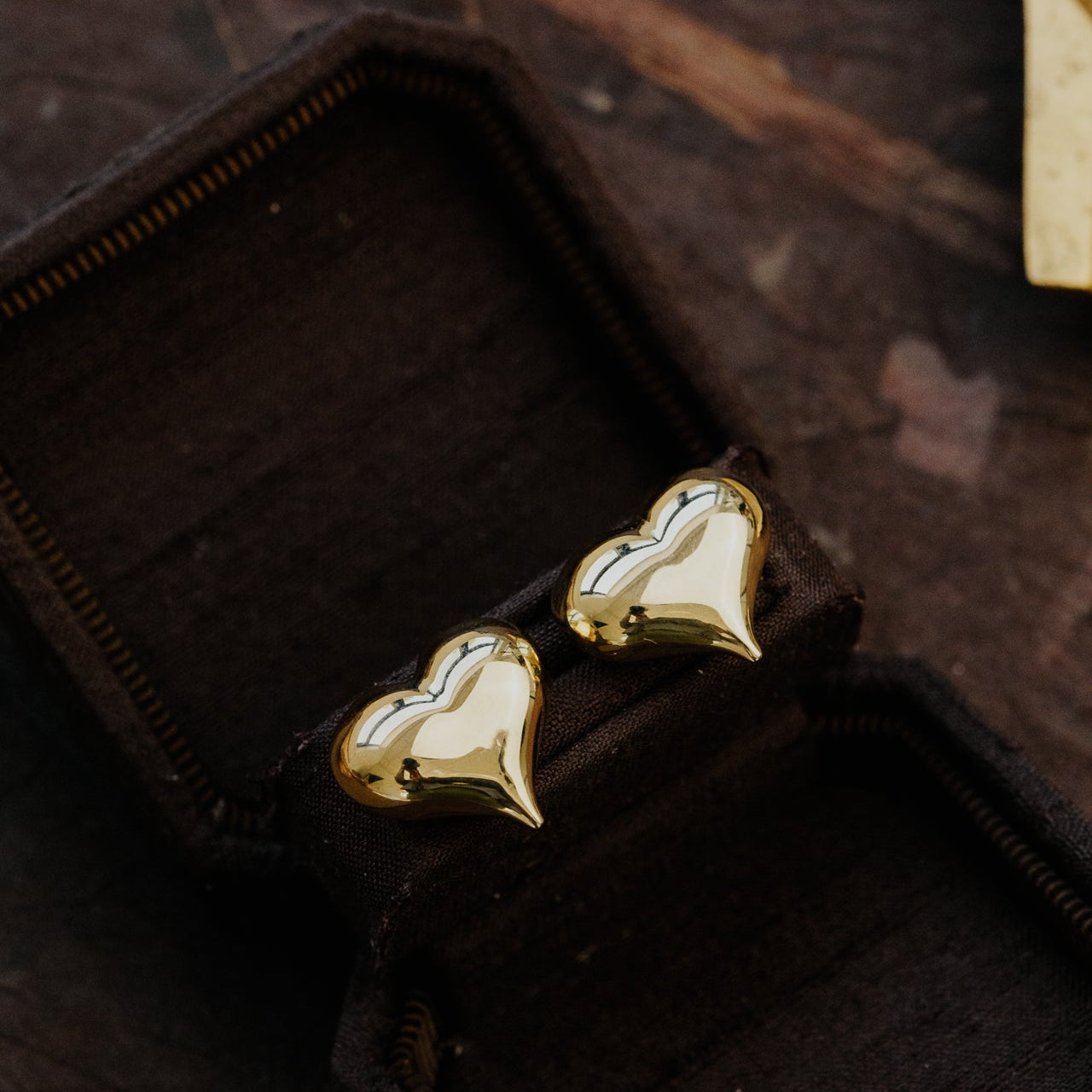 Heart-shaped gold earrings on a dark fabric background