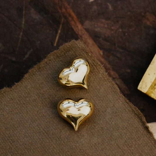 Gold heart-shaped earrings on a brown fabric background