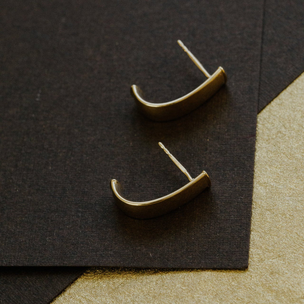 Pair of gold earrings on a black and beige geometric background