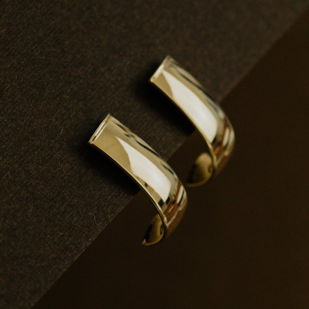 Gold hoop earrings on a dark brown surface