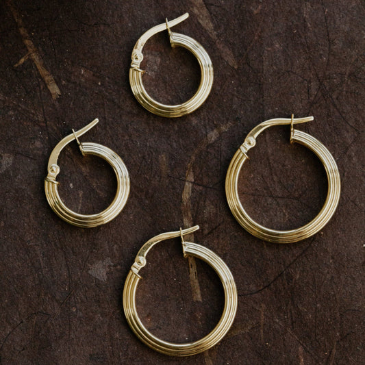 Four gold hoop earrings on a dark brown surface