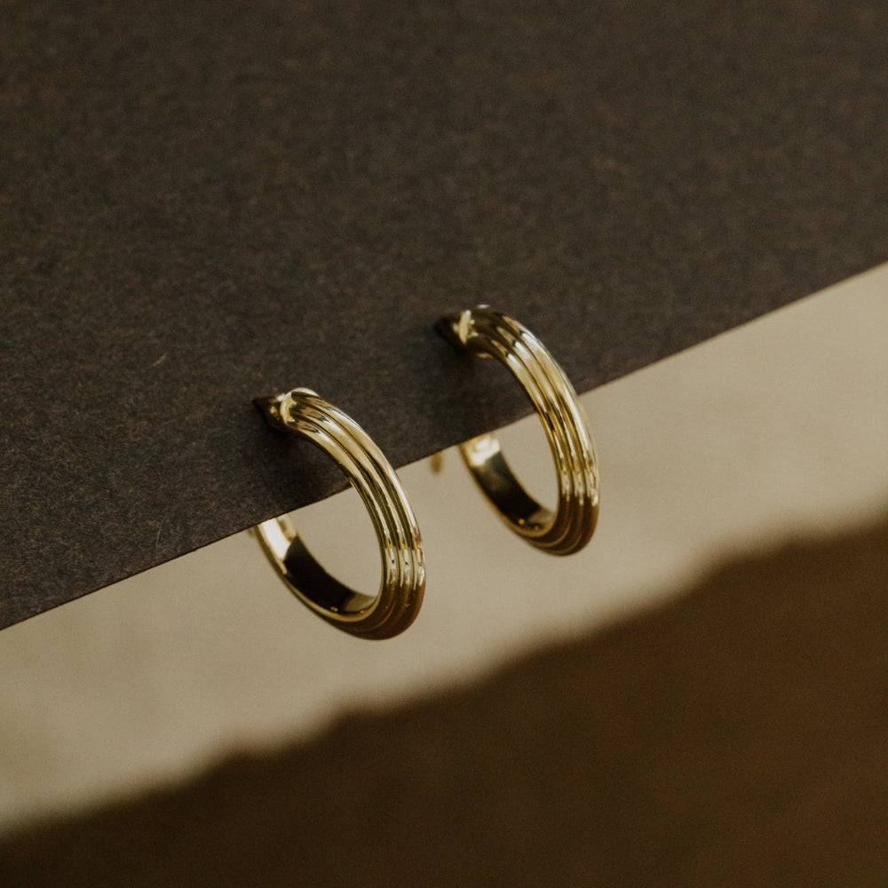 Gold hoop earrings on a dark surface with a soft shadow