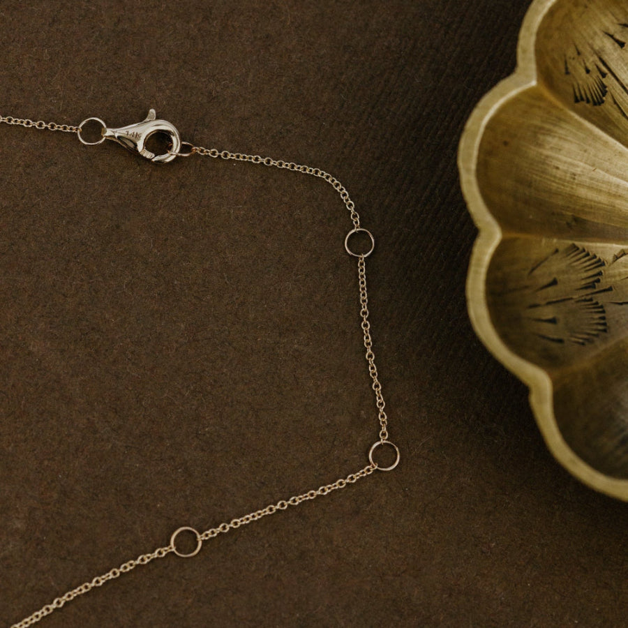 Gold chain necklace on a brown textured surface with a decorative wooden object.