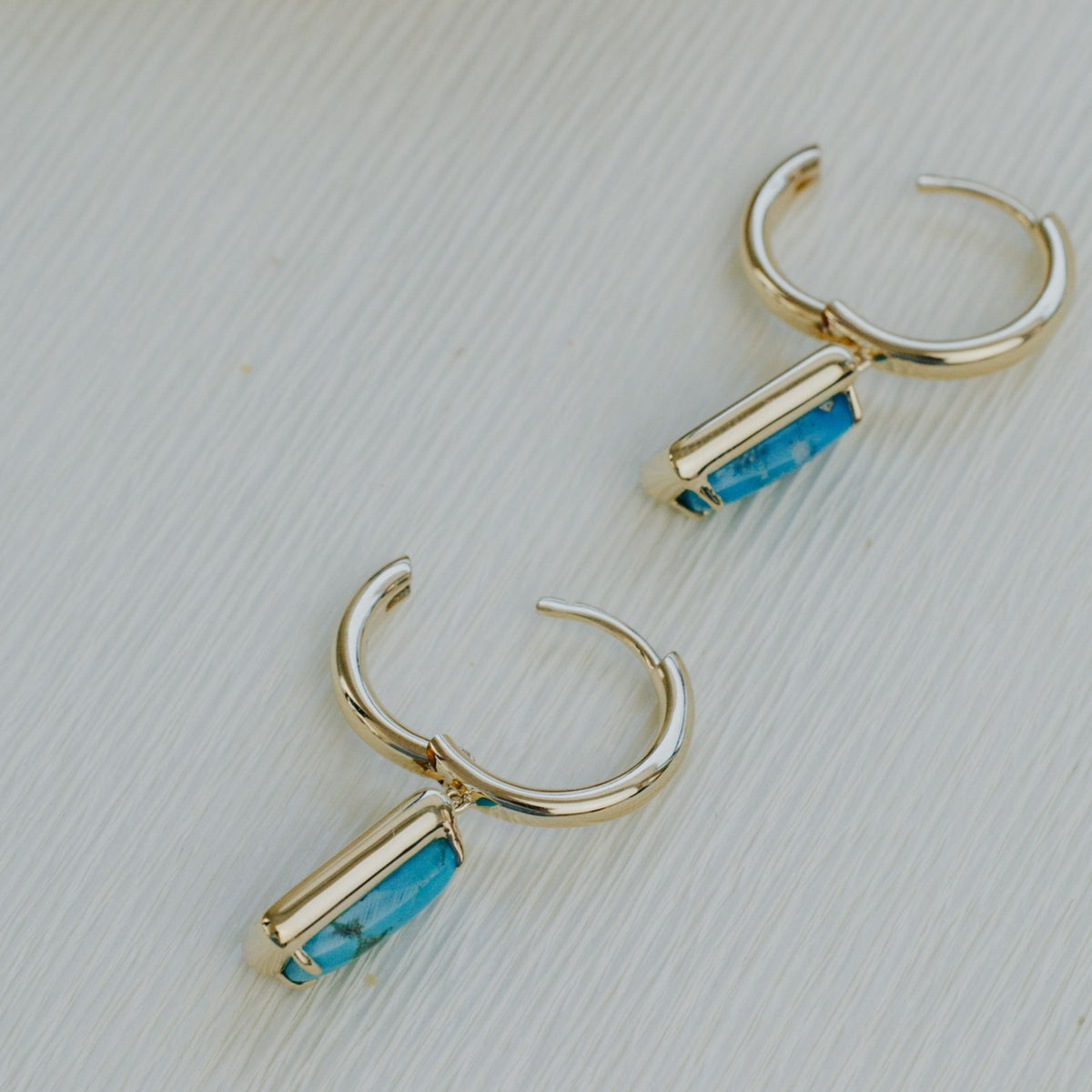 14k yellow gold rectangle turquoise dangle hoop earrings on a textured white background. 