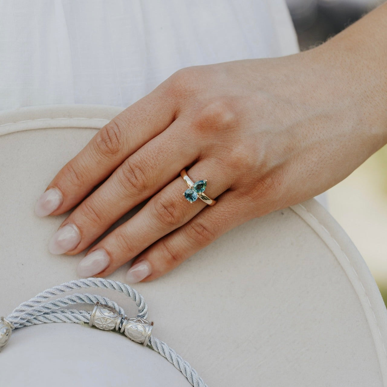 Hand wearing a ring with a green Montana sapphire gemstone on a neutral background
