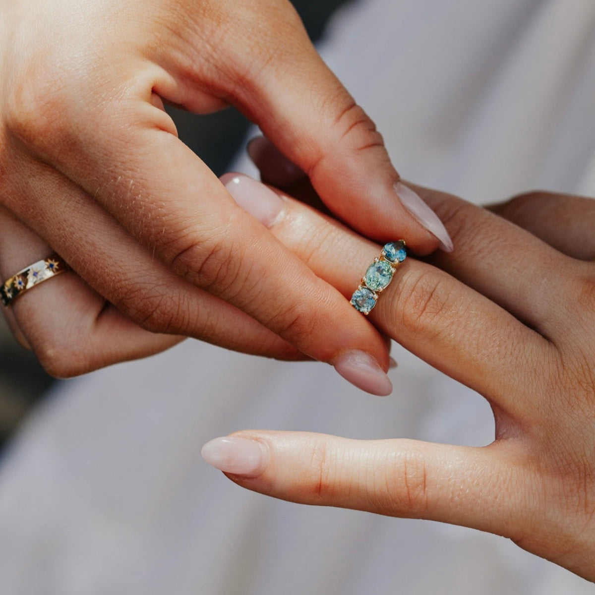 Close-up of hands with a gold Montana sapphire ring featuring blue gemstones on a blurred background