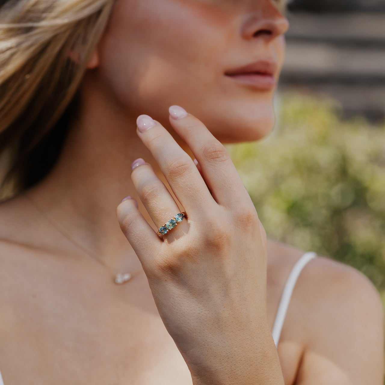 Close-up of a woman's hand wearing a green Montana Sapphire ring with a blurred outdoor background