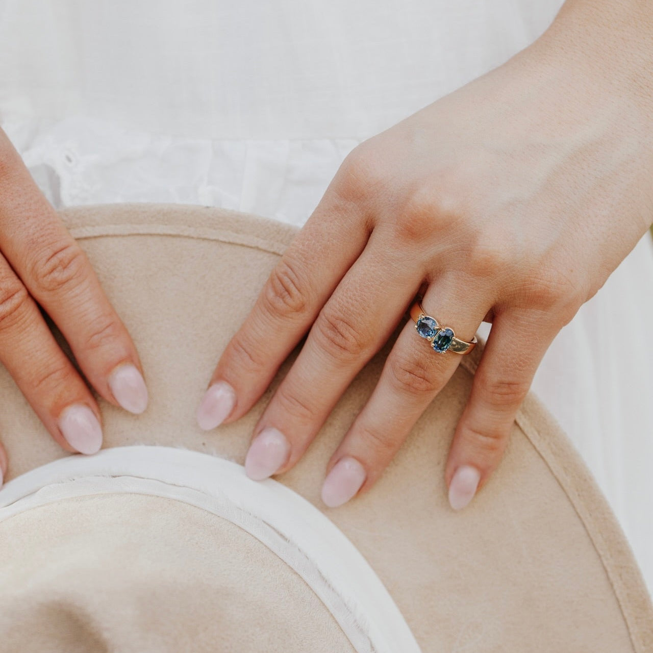 Close-up of a hand wearing a ring with a blue Montana sapphire gemstone on a beige background