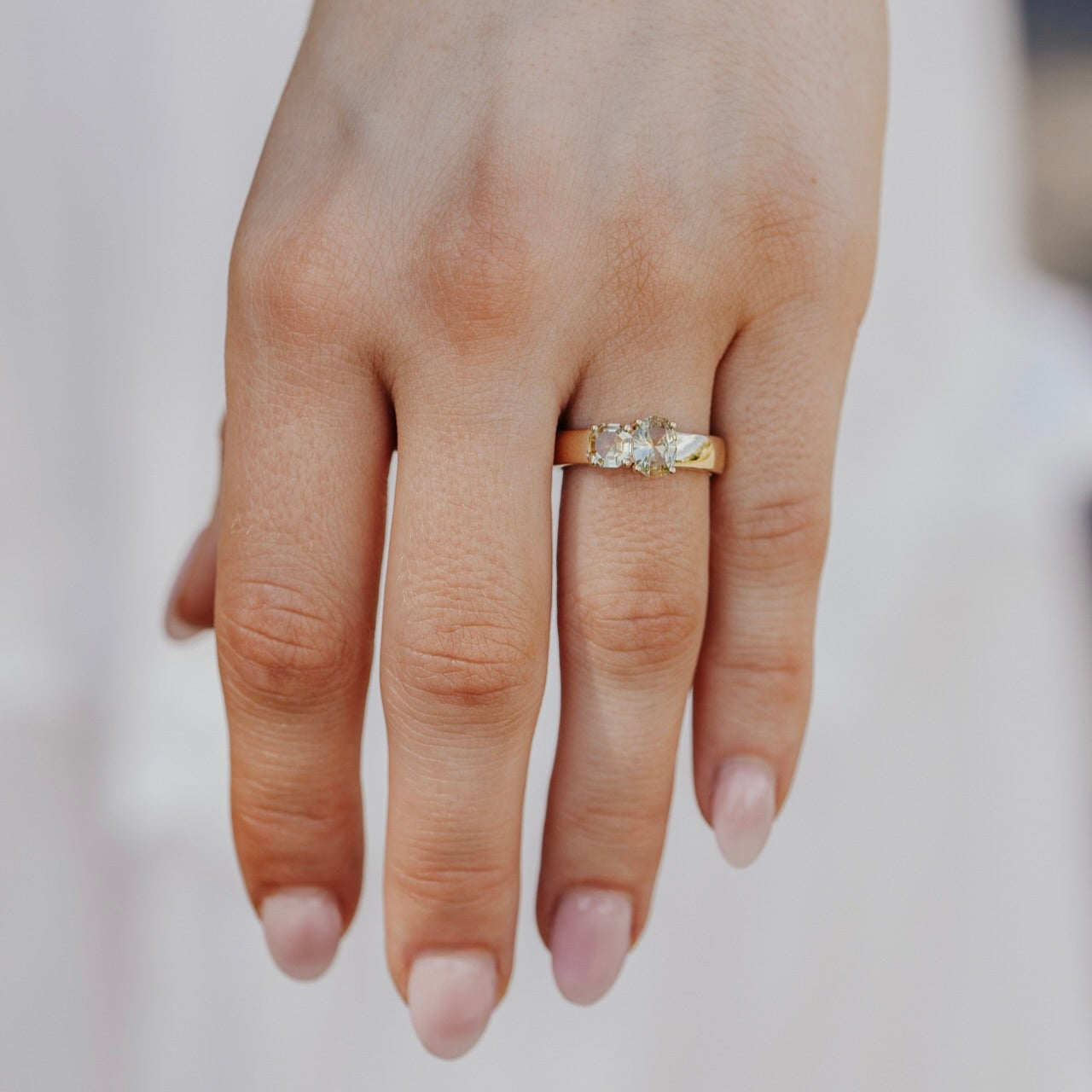 Hand wearing a gold ring with a Montana sapphire on a blurred background
