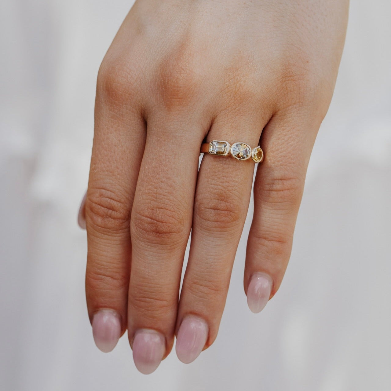 Gold ring with Montana sapphire gemstones on a person's finger against a neutral background