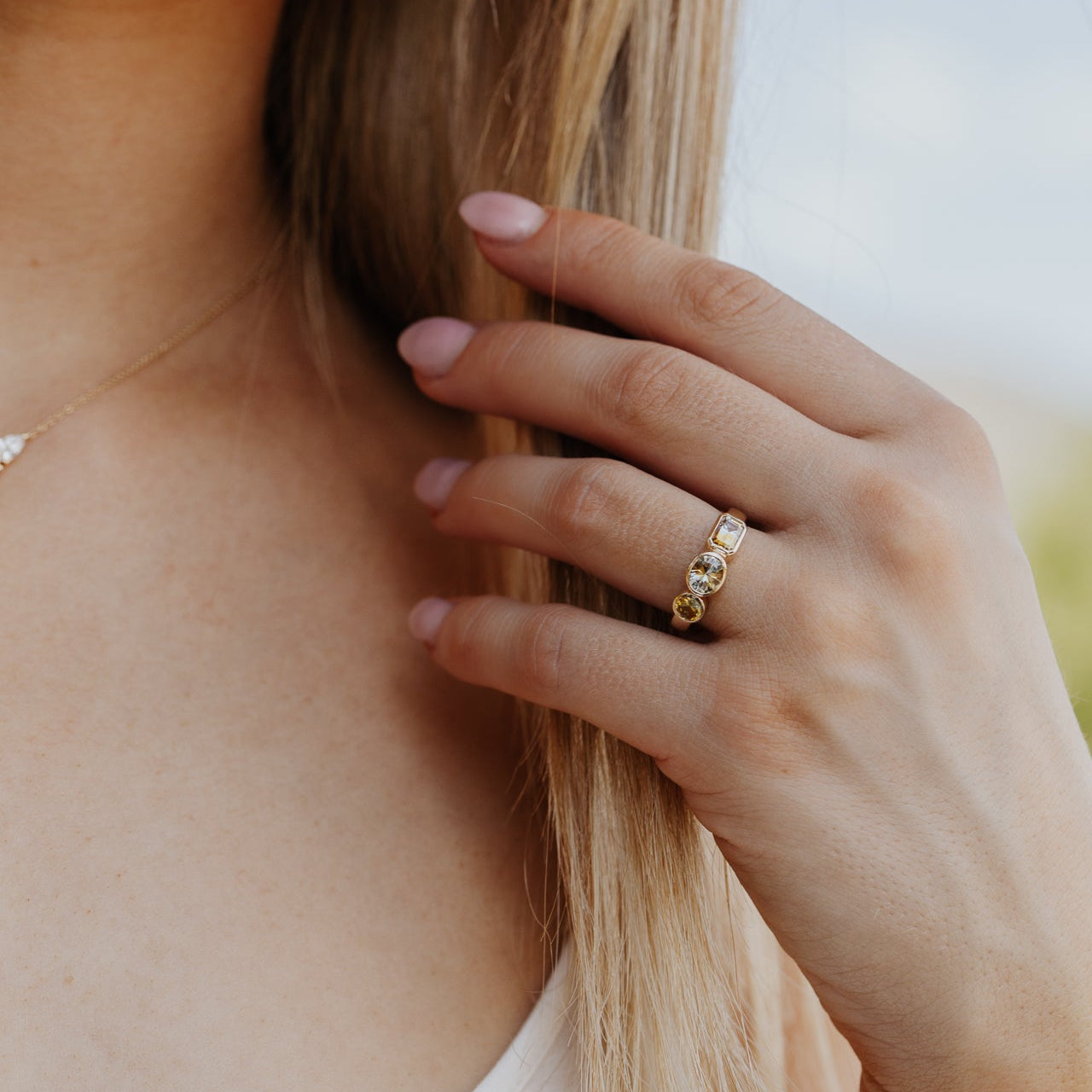 Close-up of a hand with a gold ring with Montana sapphires holding hair, with a blurred background