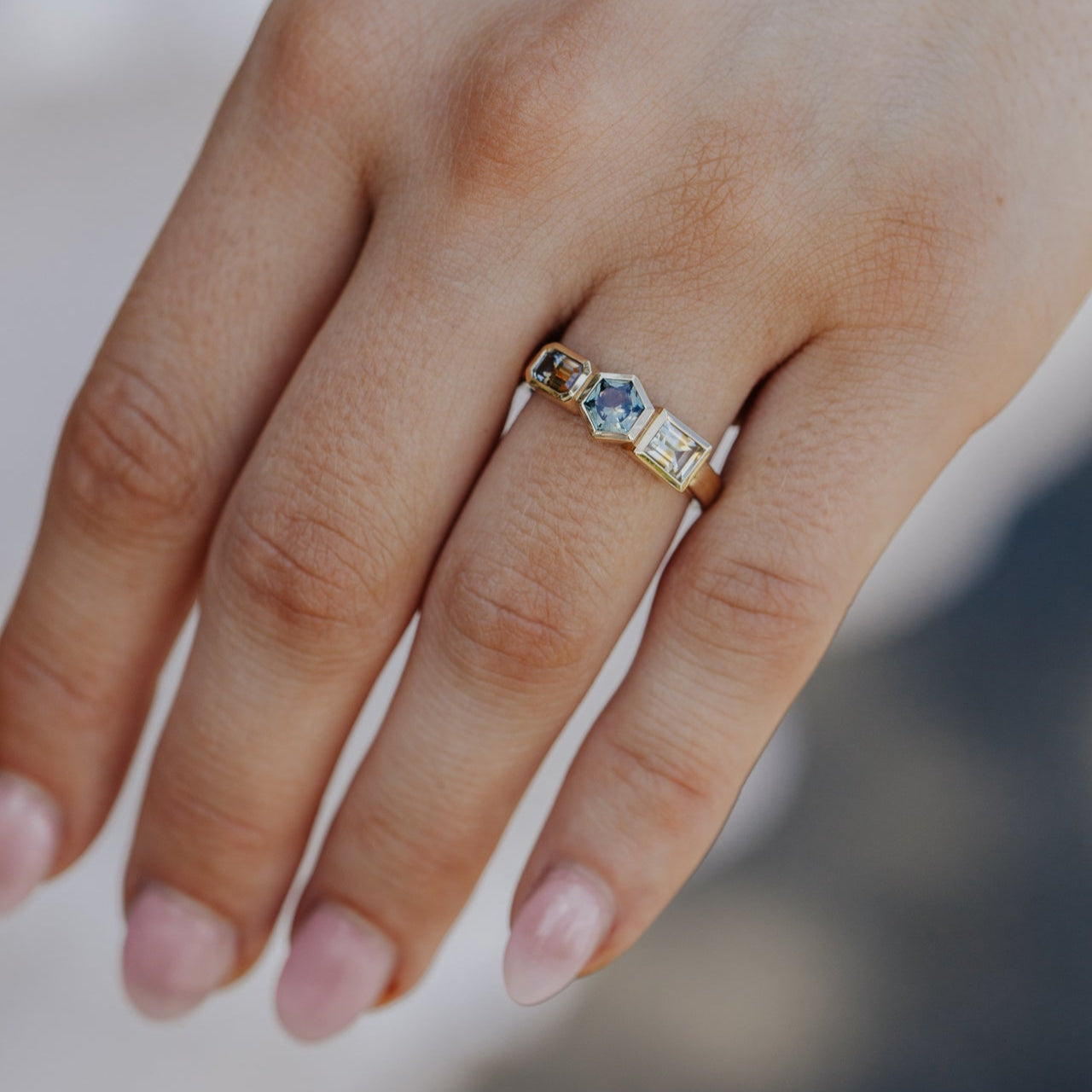 Hand wearing a gold ring with Montana sapphire gemstones on a neutral background
