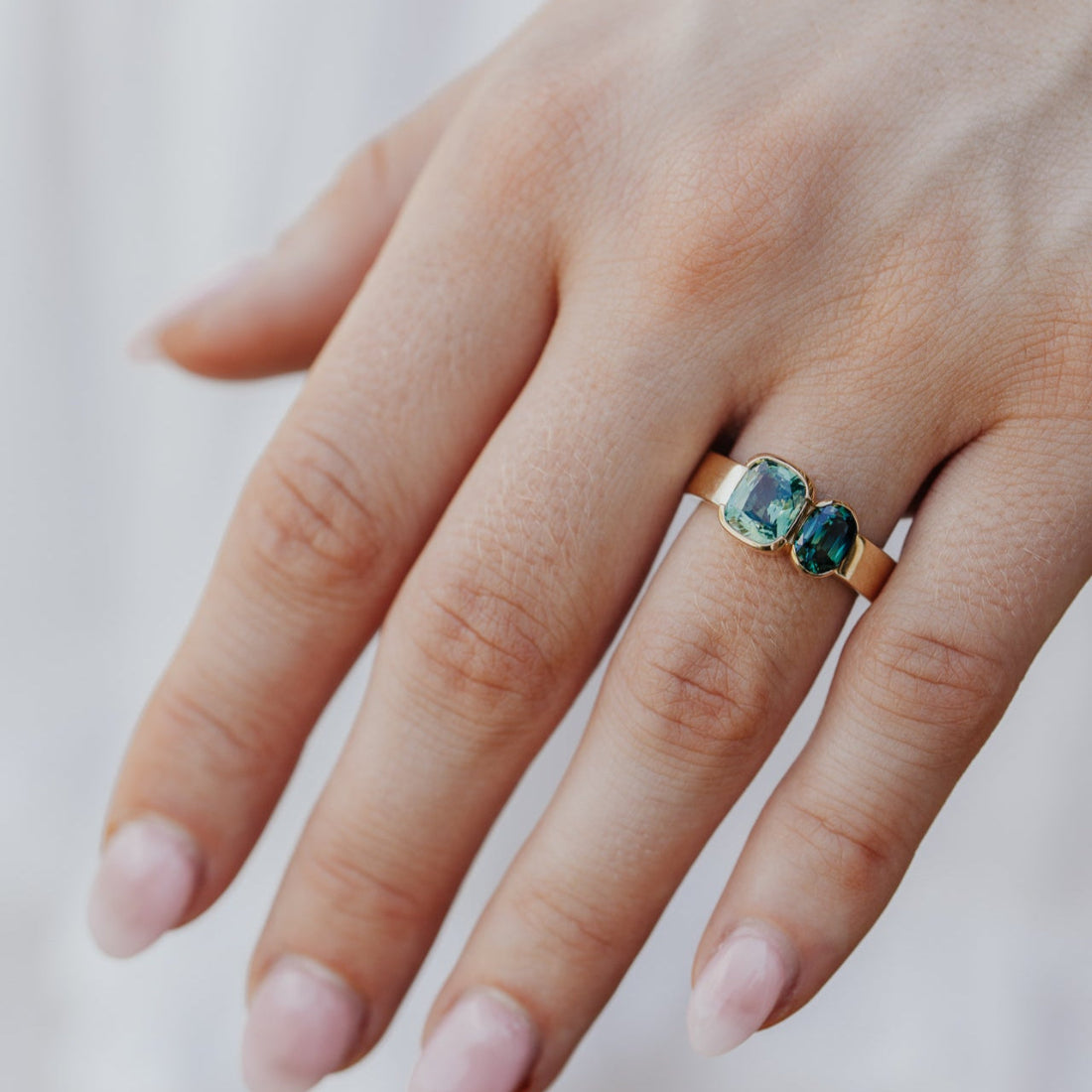 Hand wearing a gold ring with green and blue Australian sapphire  gemstone on a light background