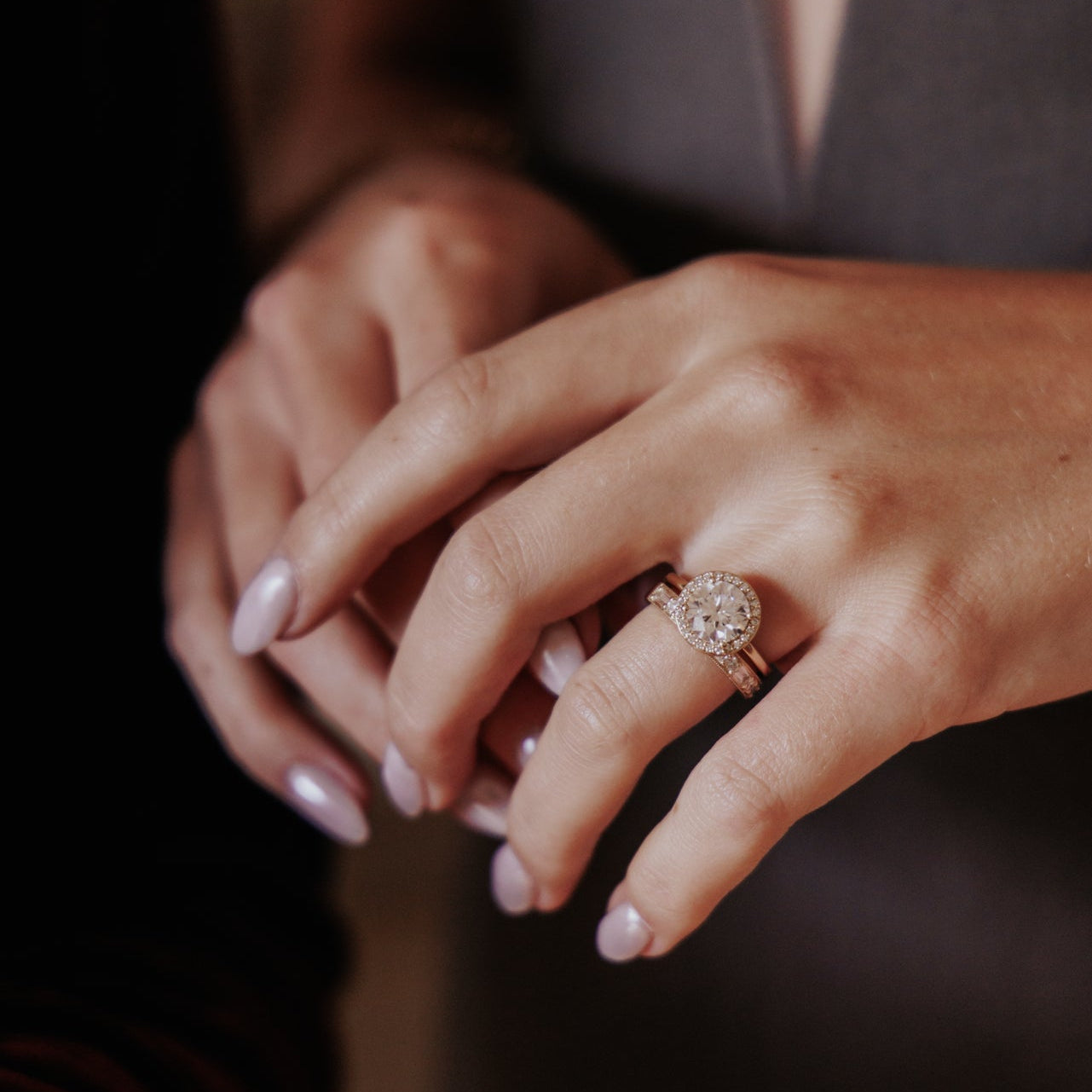 Close-up of a hand wearing a round diamond ring with a blurred background