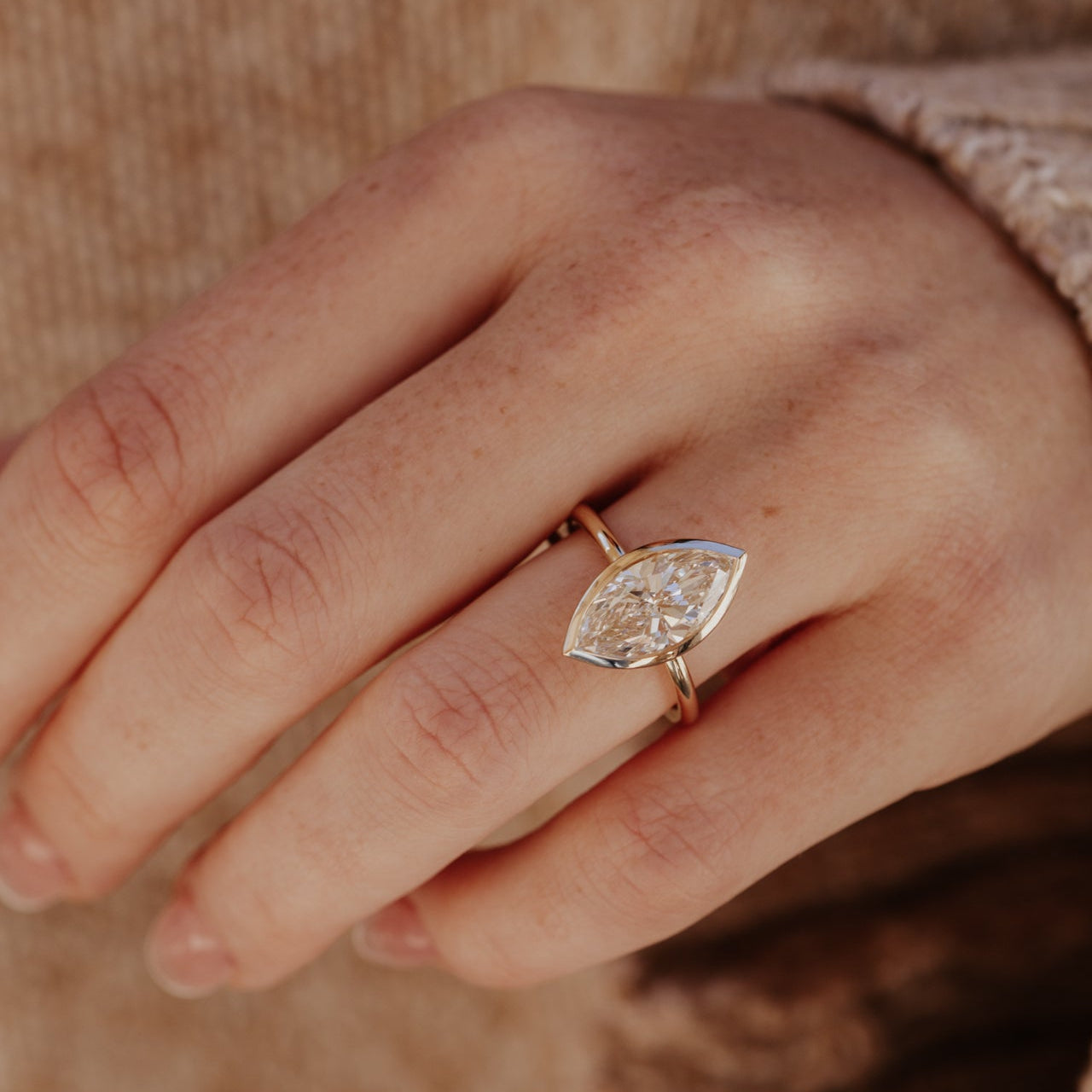 Close-up of a hand wearing a yellow gold ring with a marquise diamond on a blurred background