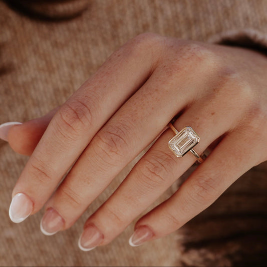 Hand wearing a emerald cut diamond ring with a blurred background