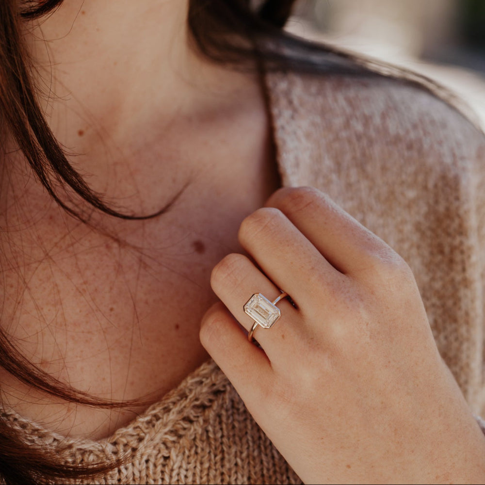 Close-up of a hand wearing a emerald cut diamond ring with a blurred background