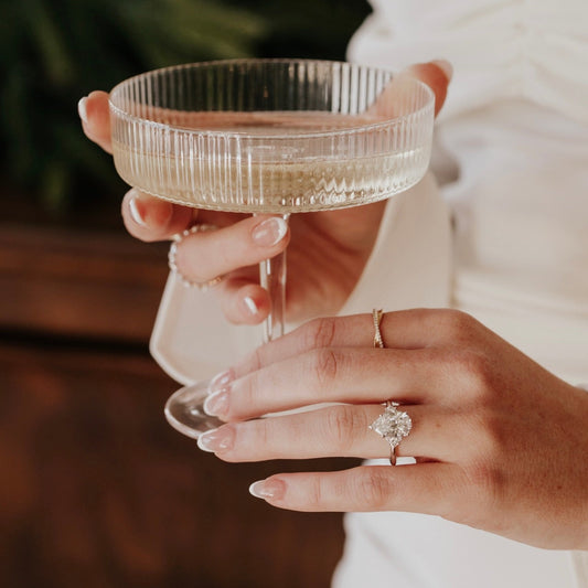 Person holding a clear glass with a blurred background wearing a pear shaped diamond ring