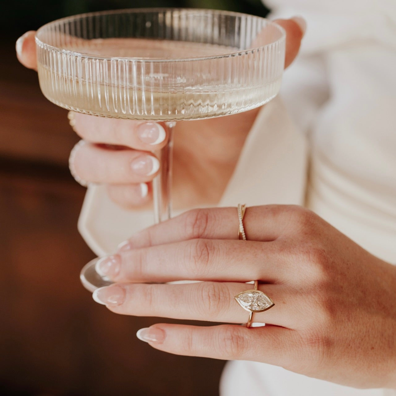 Hand holding a clear glass with a textured rim, wearing a marquise diamond ring.