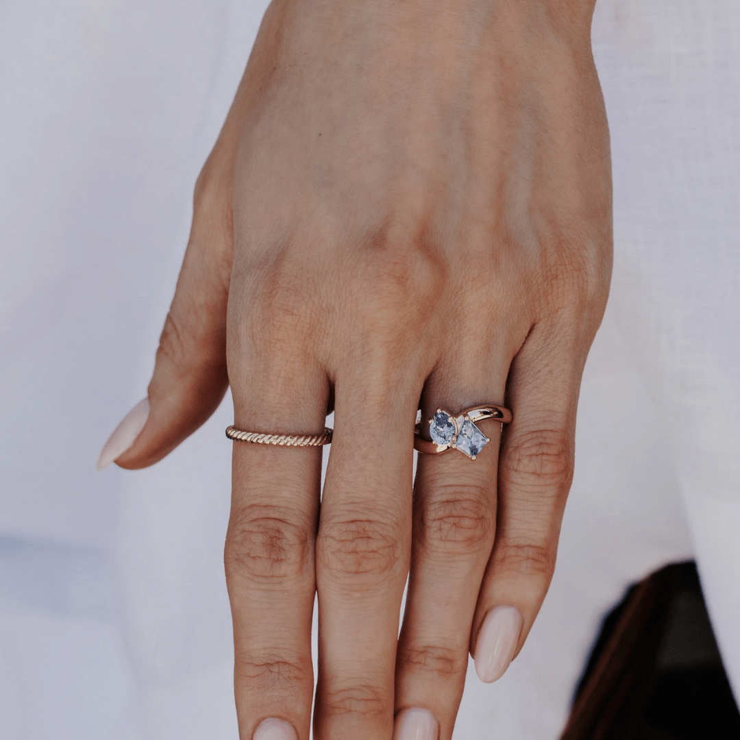 A 14k gold ring featuring kite-shaped and pear-shaped blue sapphire gemstones, displayed on the ring finger of a hand model with a soft-focus background.
