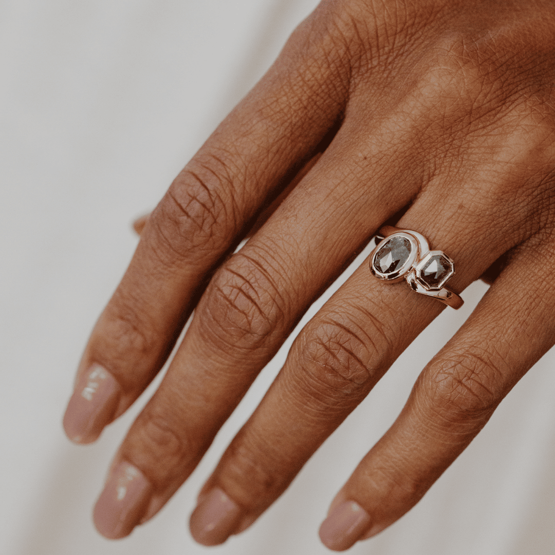 A close-up of a hand wearing a yellow gold ring with two rustic diamonds on a light neutral background.