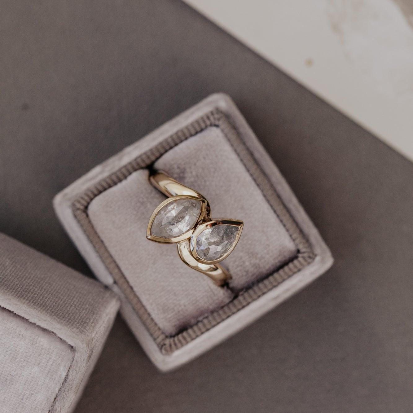 Gold ring with pear-shaped rustic diamond gemstones in a gray jewelry box.