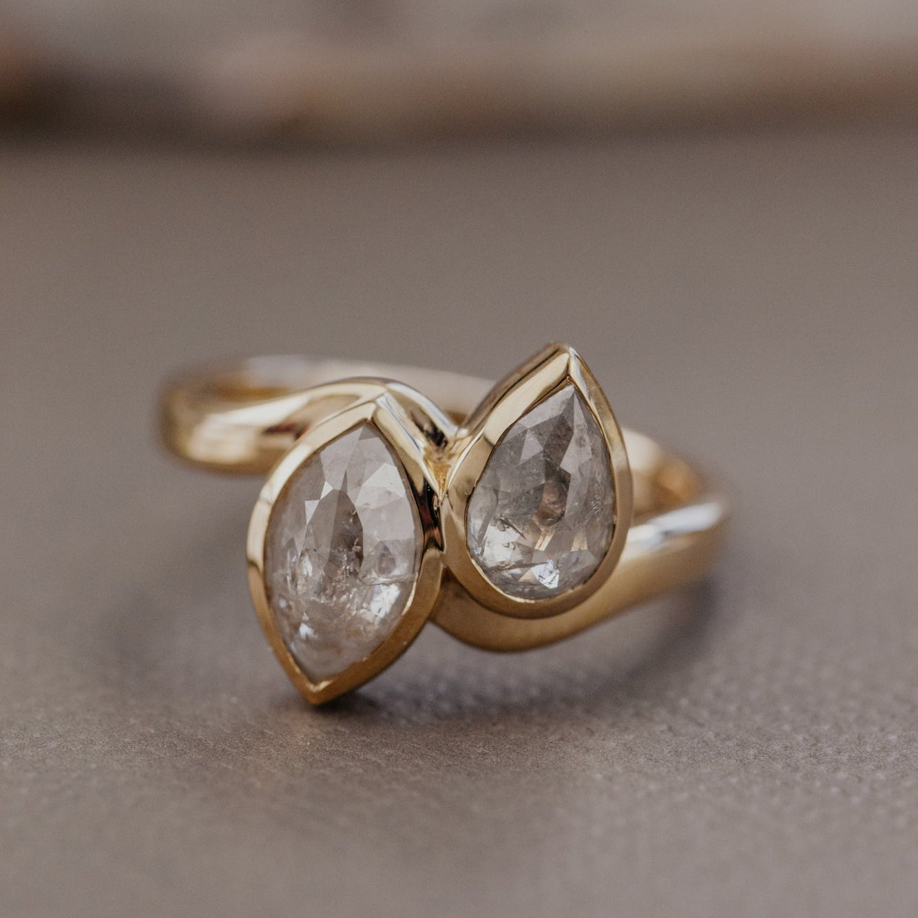 Gold ring with pear-shaped and marquise rustic diamonds diamonds on a neutral background.