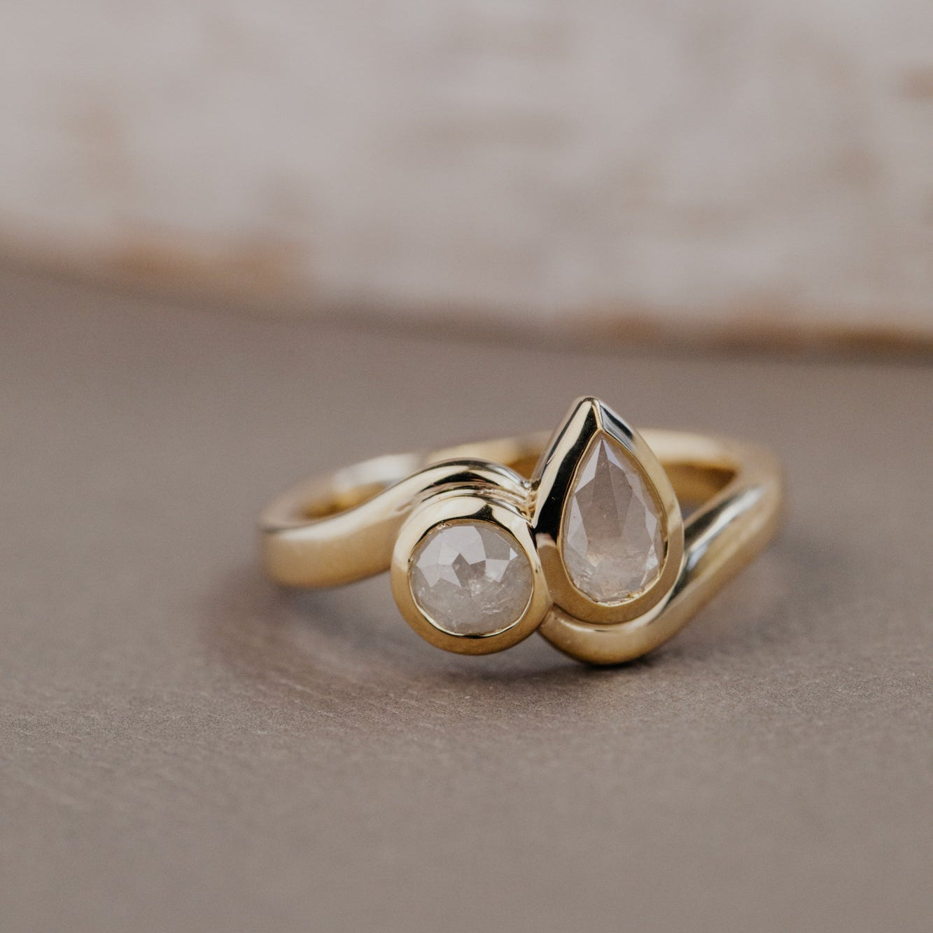 Gold Holland toi et moi ring with two rustic diamonds on a beige background.