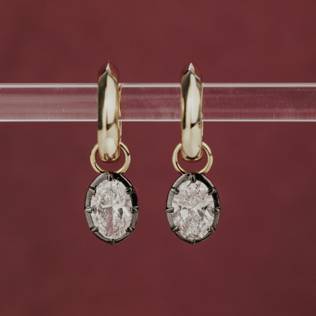 14k gold round cut, lab grown diamond dangle earrings with Black Rhodium featured on a clear tube in the center of the frame.   