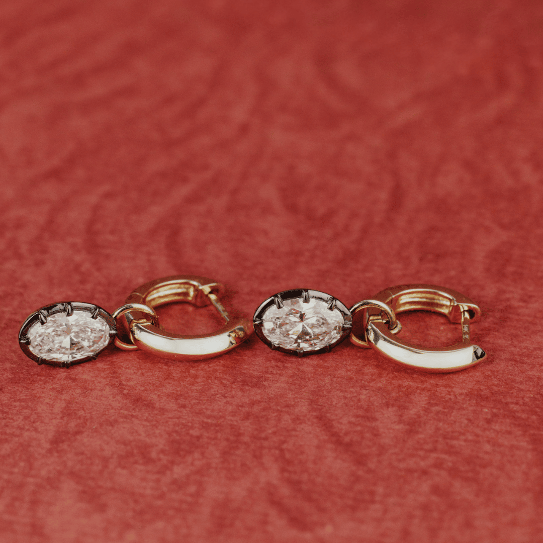 14k gold round cut, lab grown diamond dangle earrings with Black Rhodium featured on a textured red surface. 